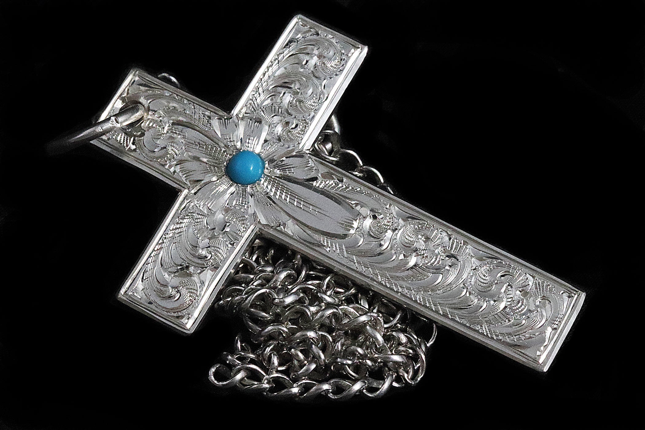 Silver cross pendant with chain and blue gemstone on a black background